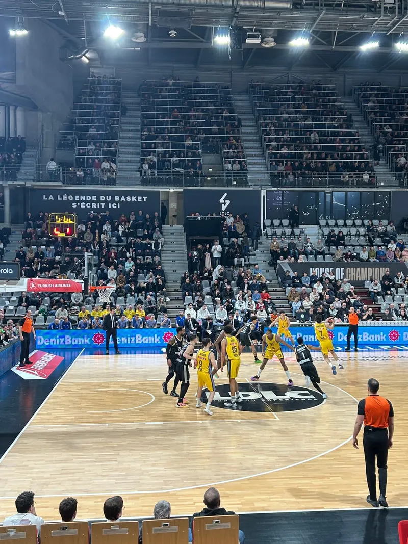A packed arena during a European league game, seen from the stands behind the baseline